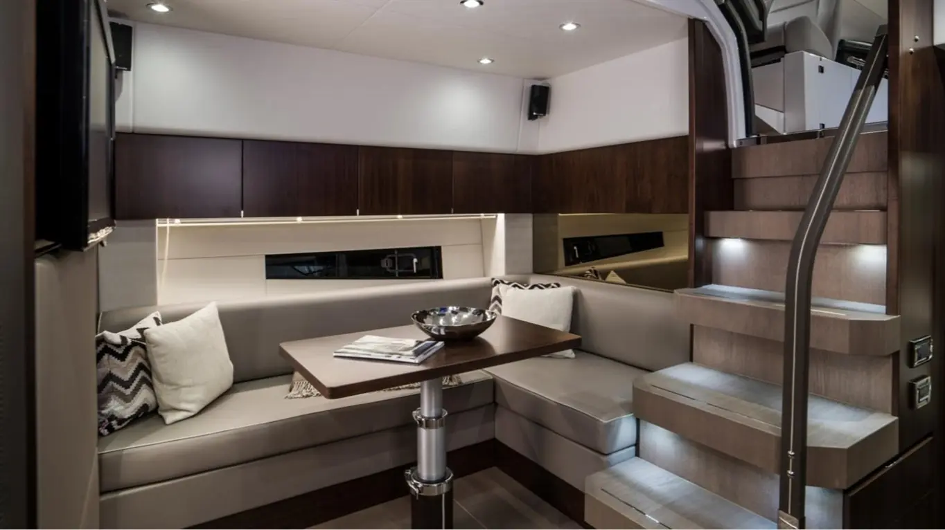 Stylish boat interior featuring a grey seating area, wooden cabinetry, a dining table, and illuminated staircase.